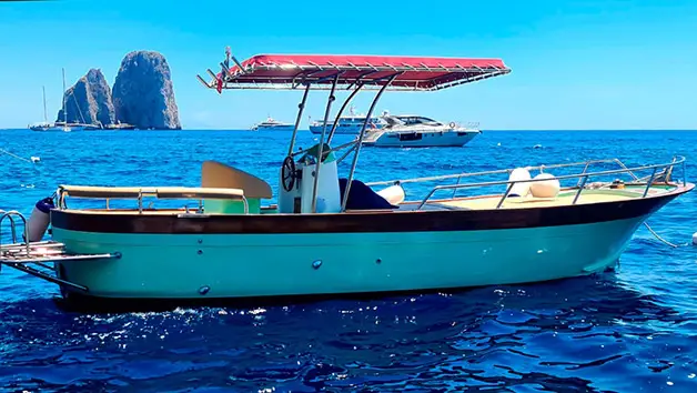 A full side-profile view of the traditional Gozzo Sorrentino boat Bellavita navigating the deep blue waters of Capri island during a private luxury charter.