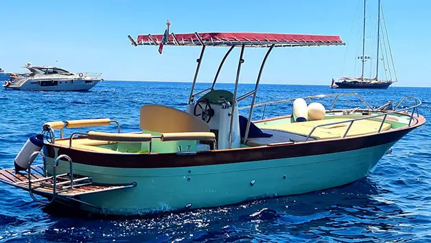 A wide stern-view of the elegant Gozzo Sorrentino boat Bellavita cruising towards the iconic vertical colorful village of Positano on the Amalfi Coast.