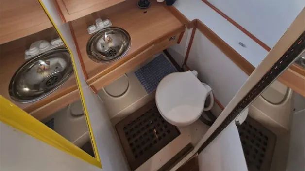 The head facility of the Wellcraft 3300, showing a wooden vanity, a sink basin, a white commode, and a drainage grate